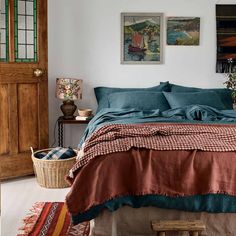 a bed with blue and brown sheets in a room next to a wooden door, rugs and pictures on the wall