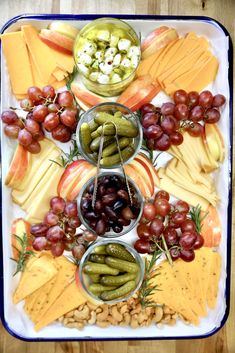 an assortment of cheeses, crackers and grapes on a platter with nuts