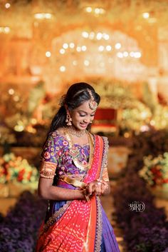 a woman in a purple and orange sari is looking down at her hand while she stands