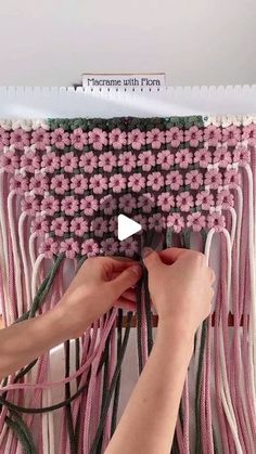 a woman is working on a piece of art with pink and white flowers hanging from the ceiling