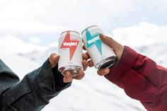 two people holding cans in their hands with mountains in the background