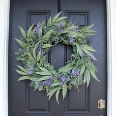 a wreath on the front door of a house with purple flowers and greenery around it