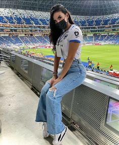 a woman wearing a face mask sitting in the stands at a soccer stadium while looking off into the distance