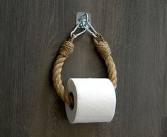 a roll of toilet paper hanging from a metal hook on a wooden wall with rope