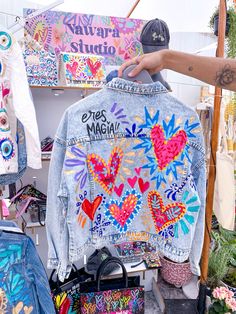 a person holding up a jean jacket that has been decorated with colorful hearts and flowers