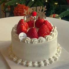 a white cake topped with strawberries on top of a table next to a christmas tree