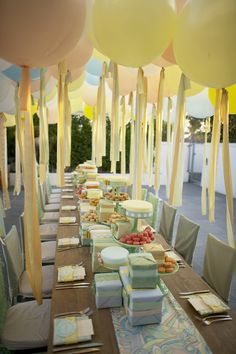 a long table covered in lots of boxes and balloons with yellow streamers hanging from the ceiling