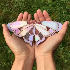 a hand holding a stained glass butterfly on it's palm in front of some grass