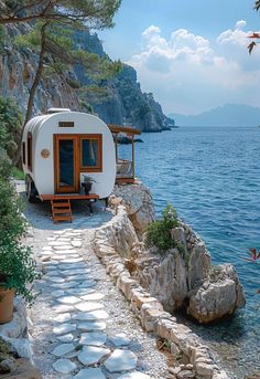 a tiny house on the edge of a cliff next to water with trees and rocks around it