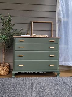 a green dresser sitting on top of a wooden floor next to a potted plant