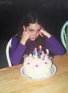 a woman sitting in front of a birthday cake with lit candles on top of it