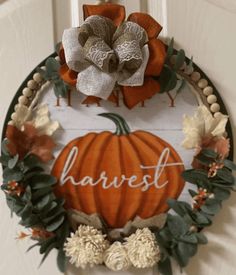 a wreath with the word harvest written on it and a pumpkin hanging from the front door