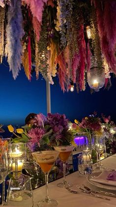 the table is set with wine glasses, candles and flowers hanging from it's ceiling