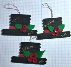 two pieces of black paper with red buttons and green leaves on them are hanging from string