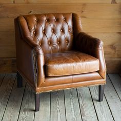 a brown leather chair sitting on top of a wooden floor next to a wood wall