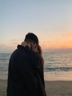 a man and woman kissing on the beach at sunset