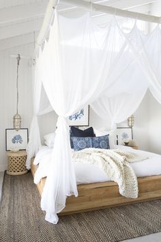 a bed with white curtains and pillows in a bedroom next to a rug on the floor