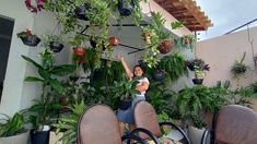 a woman standing in front of some potted plants on a patio with her arms up