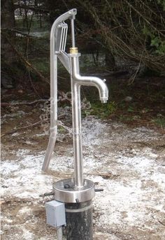 a stainless steel water pump sitting in the middle of snow covered ground next to trees