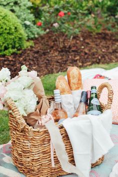 a picnic basket filled with bread, wine and other items on a blanket in the grass