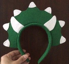 a hand holding up a green and white dinosaur hat