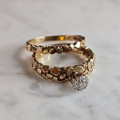 two gold rings sitting on top of a white marble counter with a diamond in the middle