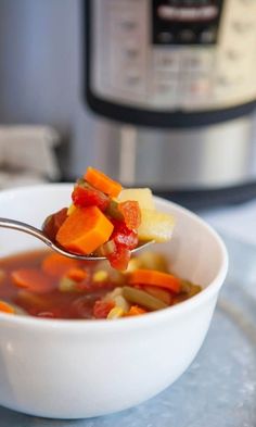 a spoon full of soup with carrots and celery in front of an instant pot