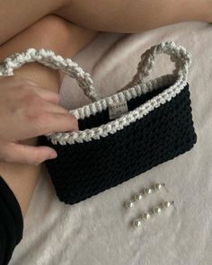 a woman is holding a black and white crochet purse with pearls on it