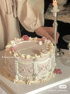 a woman is decorating a cake with white frosting and pink flowers on it