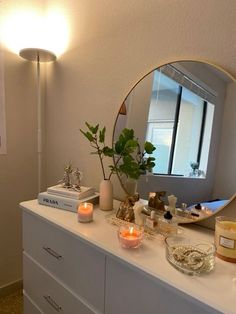 a white dresser topped with candles next to a mirror and potted plant on top of it