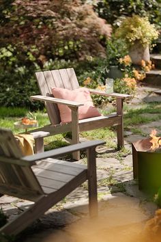 two wooden chairs sitting next to each other near a fire pit in the middle of a garden