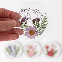 a hand holding a sticker with flowers on it and four different designs in the background