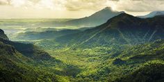 the mountains are covered in green vegetation and clouds above them, as seen from an overlook point