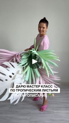 a woman is holding a large bird made out of paper and plastic leaves in front of her face