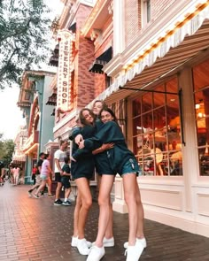 two young women hugging each other in front of a building on a city street with people walking by