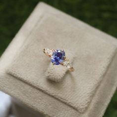 an engagement ring with blue and white stones sits on top of a cloth box in the grass