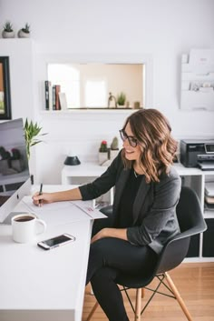 a woman sitting at a desk with a cup of coffee and cell phone in her hand