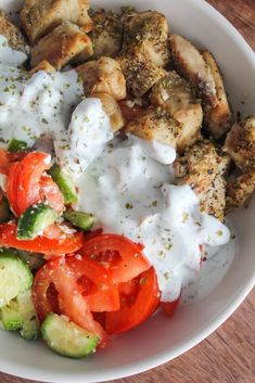 a white bowl filled with chicken, tomatoes, cucumbers and tzatzh