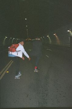 two people are skateboarding down the street at night time, one is carrying a backpack