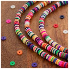 multicolored beaded necklaces are laying on a wooden surface and scattered with colorful beads