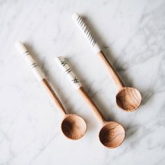 three wooden spoons and two white toothbrushes on a marble surface