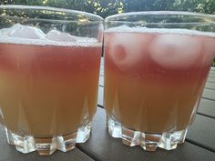 two glasses filled with liquid sitting on top of a wooden table next to each other