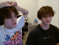 two young men sitting next to each other in front of a computer screen and one is holding his head