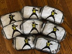 six packages of white frosted donuts with black and yellow images on them, sitting on a wooden table