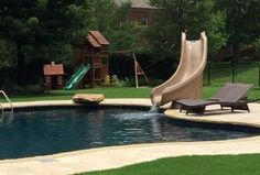 a pool with a slide in the middle and some lawn chairs around it on the other side