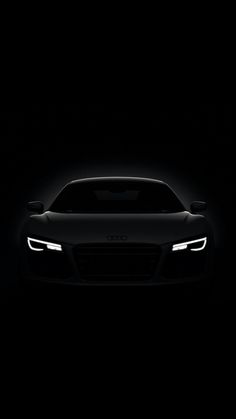 the front end of a black sports car with headlights on in the dark night time