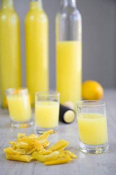 two glasses filled with yellow liquid next to some sliced oranges