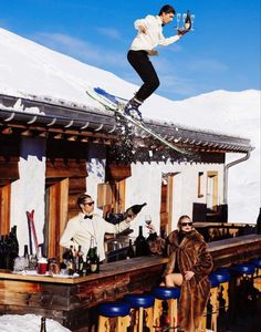 a man flying through the air while riding skis on top of a bar next to a woman