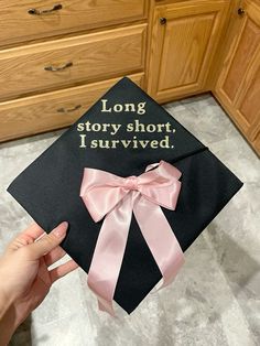 a graduation cap that says long story short, i survived with pink ribbon on it