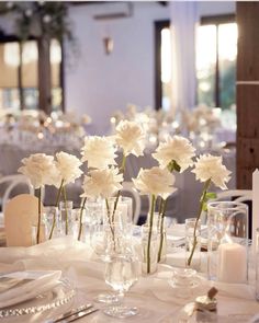 white flowers are in vases on a table with silverware and place settings for dinner